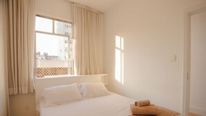 Un dormitorio con cama, ventana con cortinas y suelo de madera.