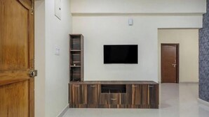 Un salon avec un téléviseur à écran plat fixé au mur, un meuble de rangement en bois et une porte sur le côté gauche.