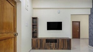 Sala de estar con televisor de pantalla plana montado en la pared, mueble de entretenimiento de madera y una puerta a la izquierda.