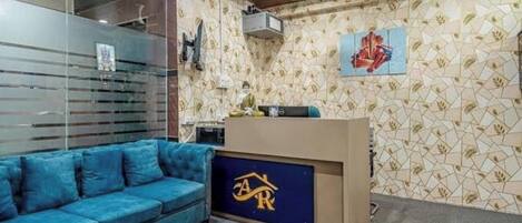 A room with a blue sofa, a wooden ceiling, a patterned wall, and a logo on the desk.