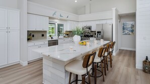A spacious kitchen with white cabinetry, a large island with bar stools, and a view of the outdoors.