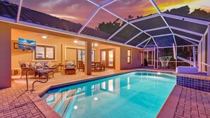 A swimming pool with a covered area, lounge chairs, and a television screen.