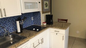 A kitchen with white cabinets, a granite countertop, a microwave, a coffee maker, and a sink.