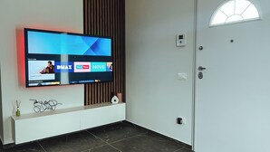 Een moderne woonkamer met een flatscreen televisie aan de muur, een witte console tafel en een deur met een raam.