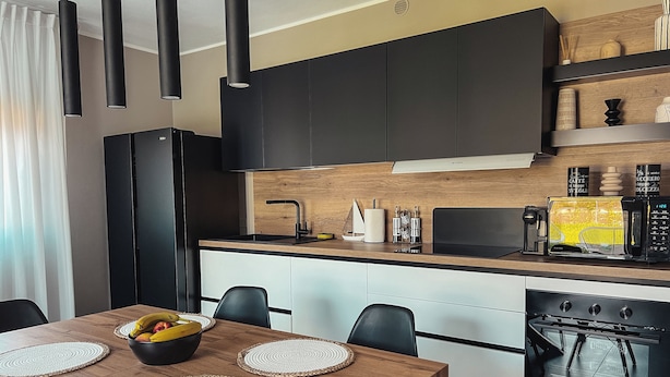 Een moderne keuken met zwarte kastjes, een houten aanrechtblad en een eethoek met een houten tafel en stoelen.