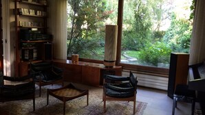 A spacious living room with a large window, a bookshelf, two leather chairs, a coffee table, and a piano. - Architect-designed villa in a garden paradise with 13x6 pool and tennis court (saint-jean)