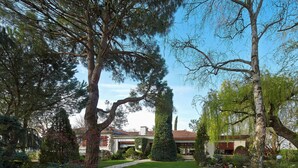 A well-maintained garden with a variety of trees and shrubs, a stone pathway, and a building with a red roof in the background. - Architect-designed villa in a garden paradise with 13x6 pool and tennis court (saint-jean)