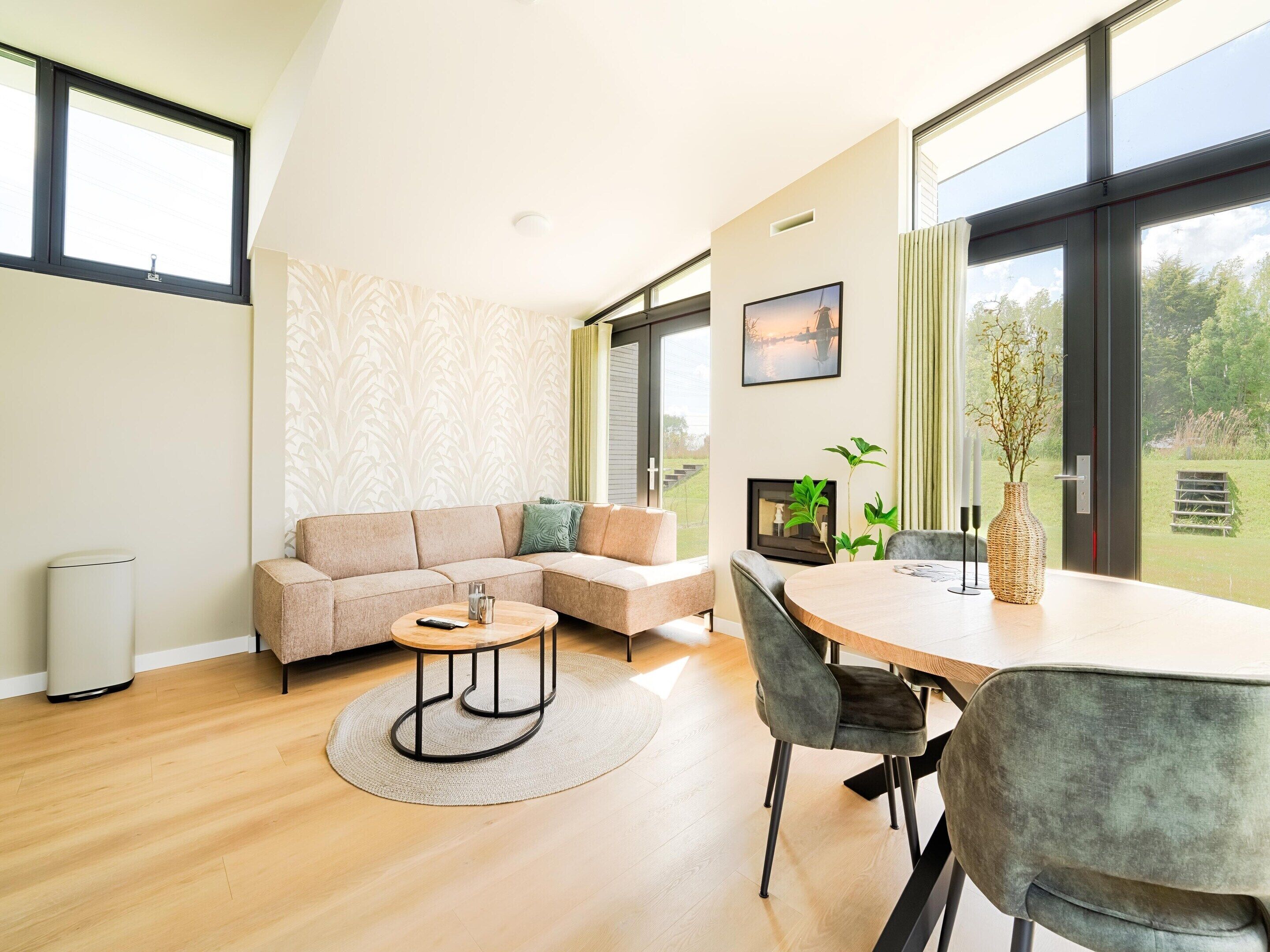 Uma sala de estar moderna com sofá, mesa de centro e mesa de jantar. Há janelas amplas e vista para o exterior.