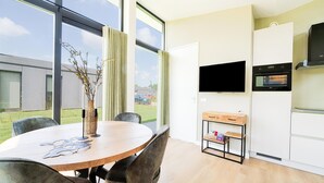 Une cuisine moderne dotée d’un four encastré, d’un téléviseur fixé au-dessus du four, et d’un coin repas avec une table ronde et des chaises.