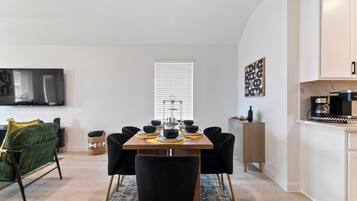 Un espace repas moderne avec une table en bois, des chaises noires et une machine à café.