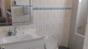 Un baño con inodoro, lavamanos, espejo y paredes con azulejos.