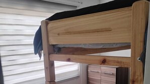 Una cama litera con estructura de madera, colchón negro y un pequeño cajón.