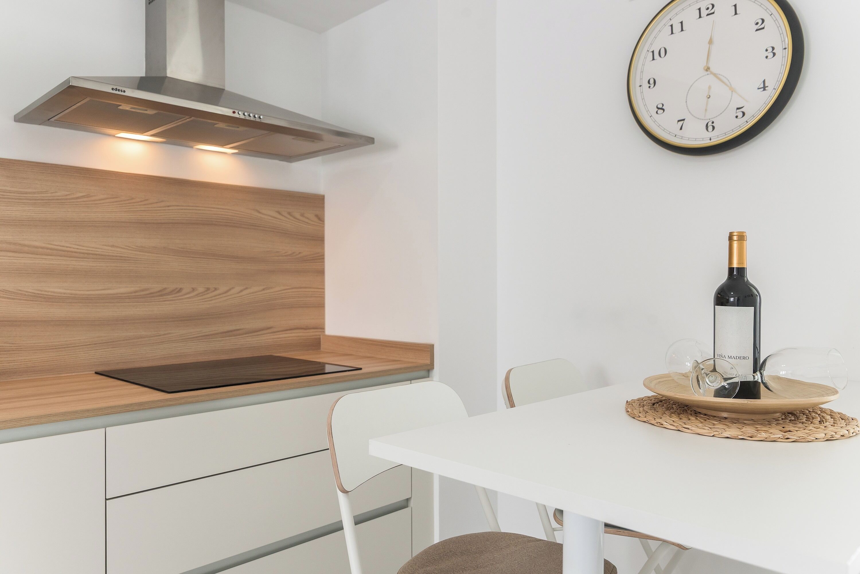 A modern kitchen with a built-in stove, wooden countertop, and a dining area with a white table and chairs.