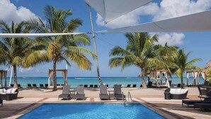 A poolside area with lounge chairs, palm trees, and a view of the ocean.