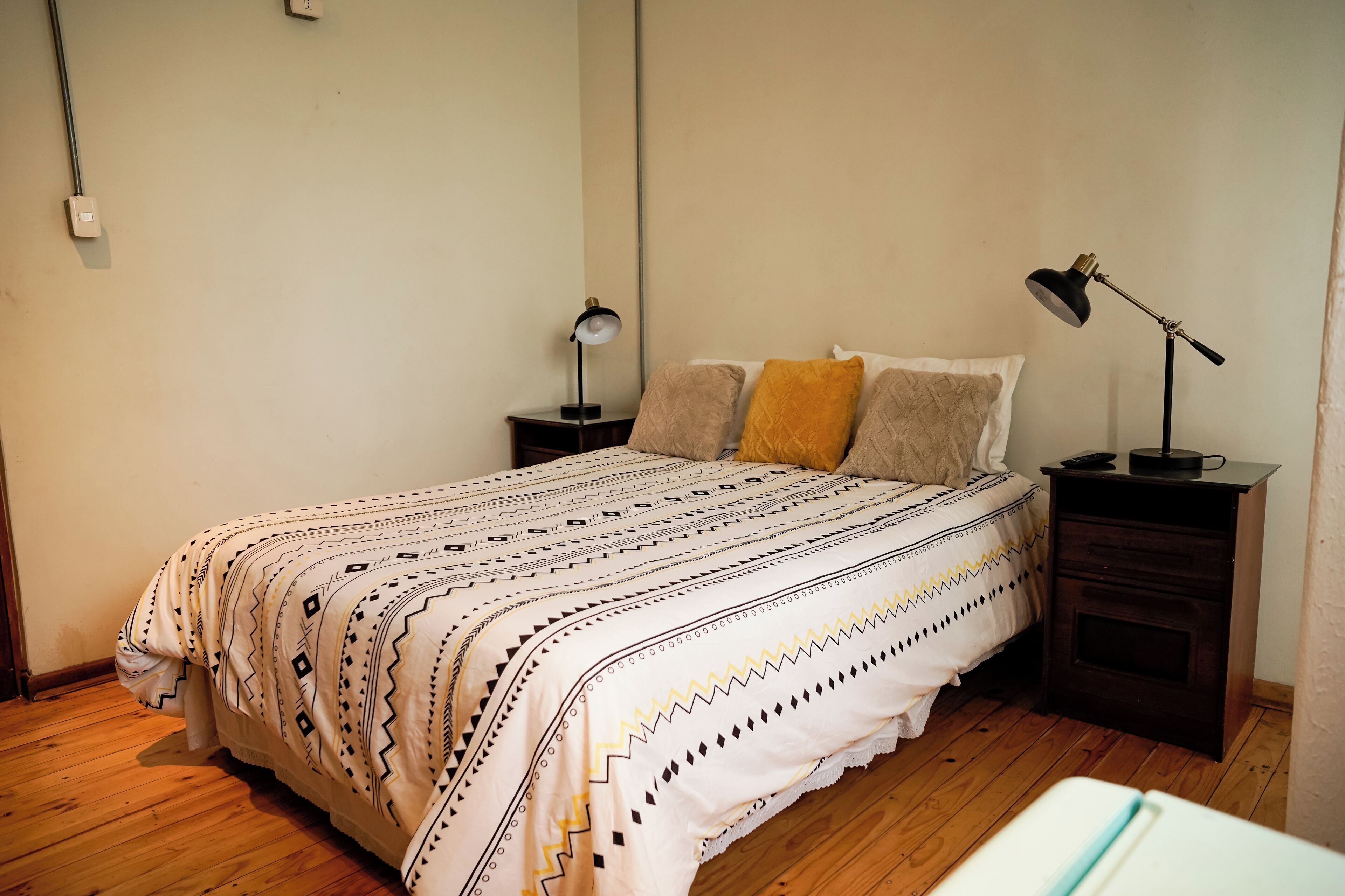 Un dormitorio con una cama, dos mesitas de noche, una lámpara y suelo de madera.