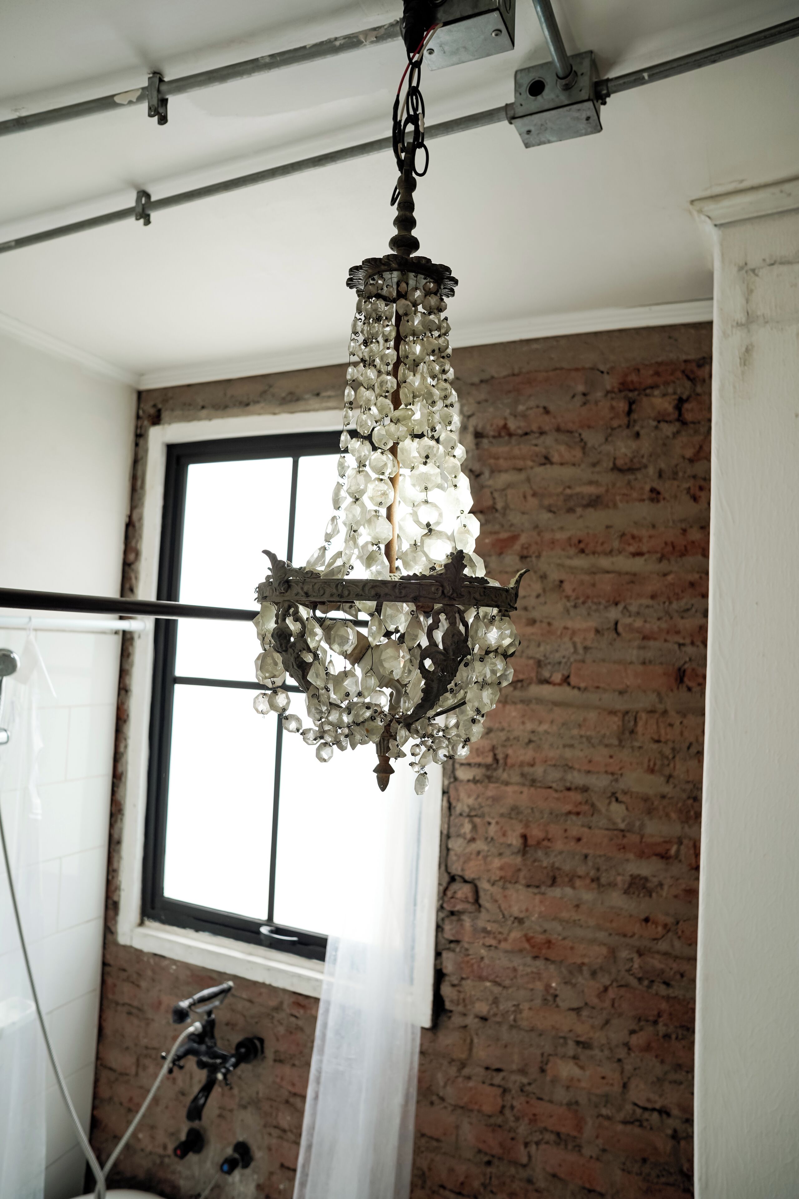 A chandelier in a room with exposed brick walls and a window.