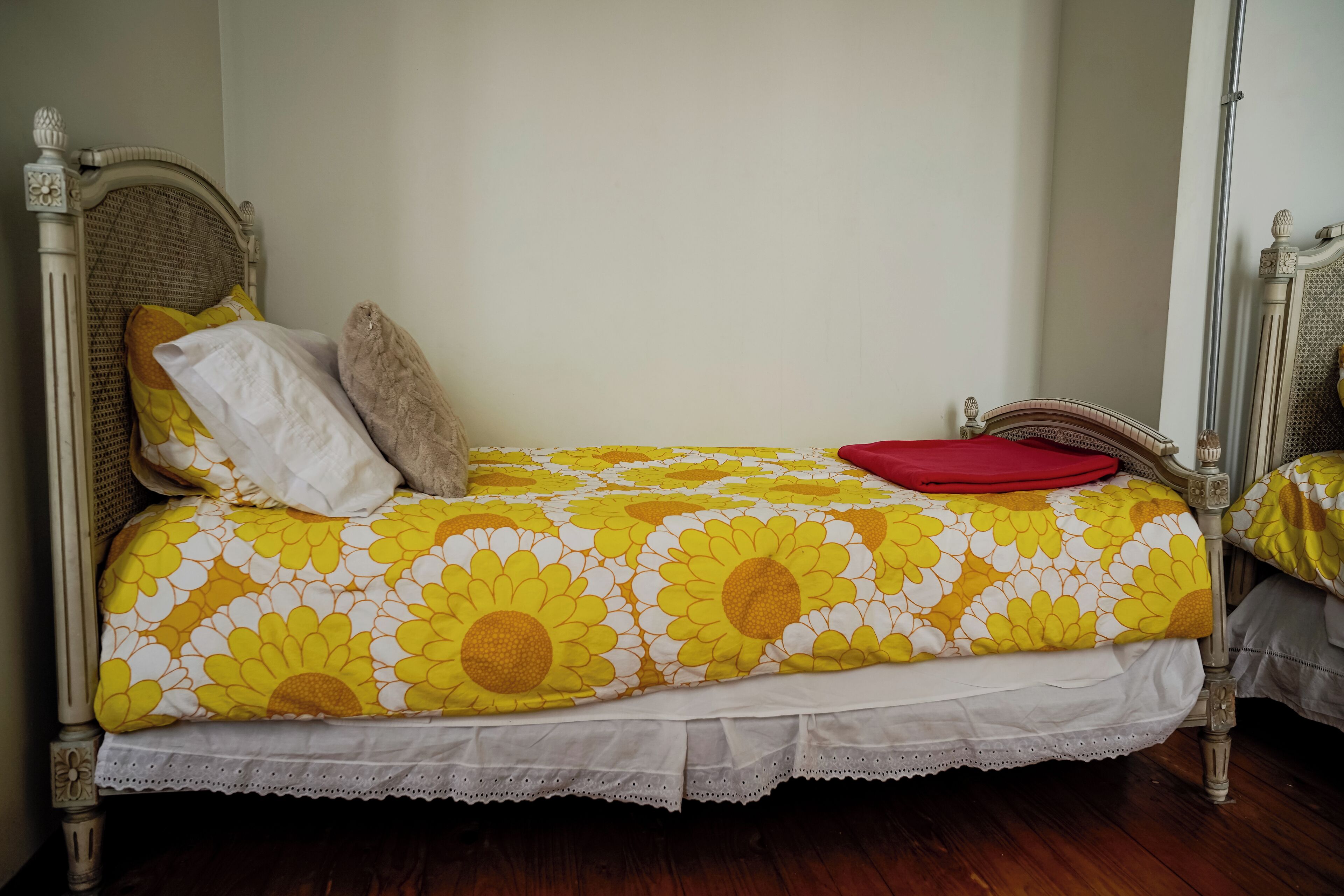 Una cama individual con cubrecolchón floral, un reposapiés de encaje blanco y un cabecero de madera.