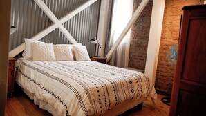 A bedroom with a bed, a wooden nightstand, a lamp, and a brick wall.