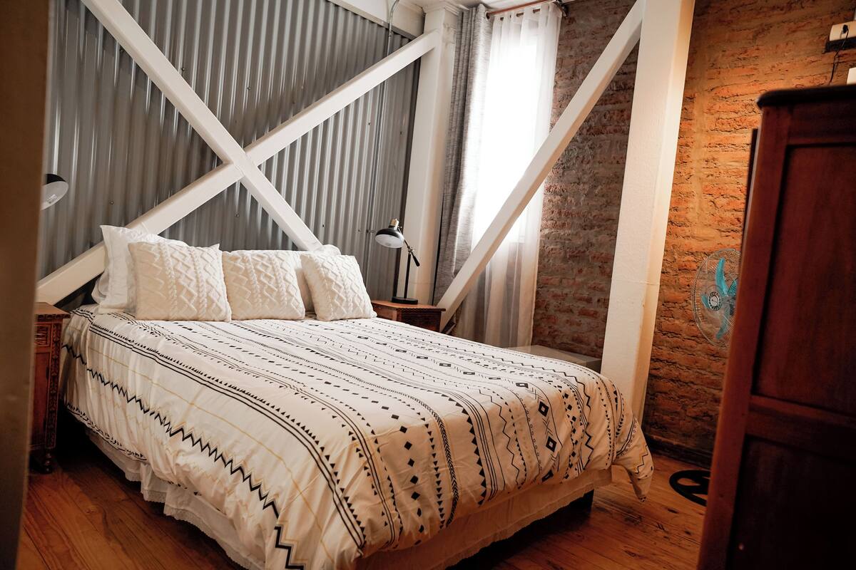 Una camera da letto con un letto, un comodino in legno, una lampada e una parete in mattoni.