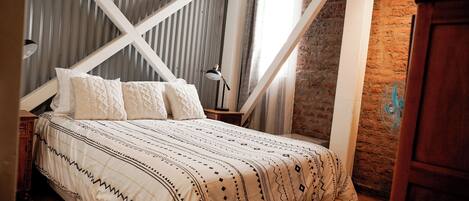 A bedroom with a bed, a wooden nightstand, a lamp, and a brick wall.