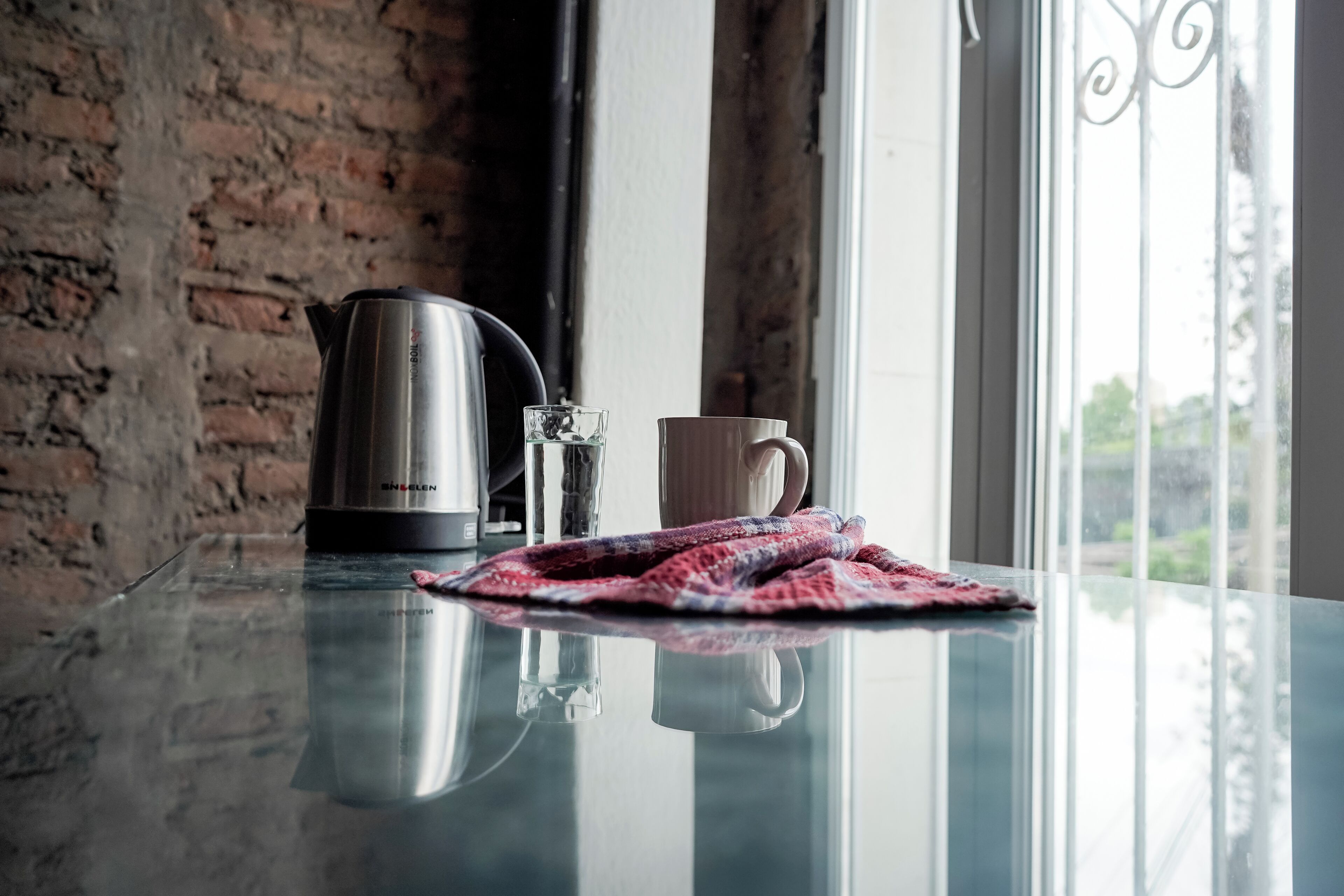 A kitchen counter with a stainless steel kettle, a glass, and a mug.