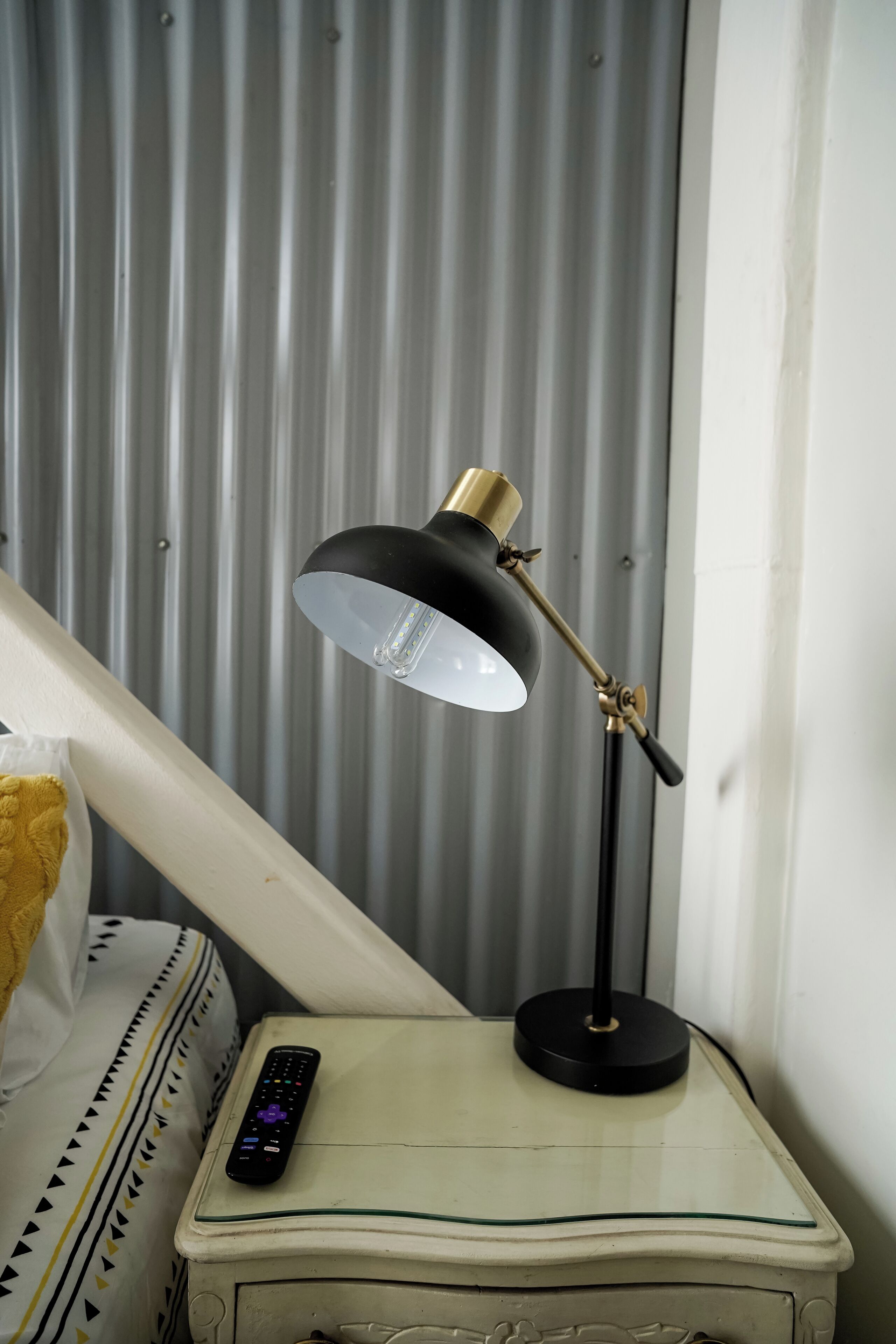 A bedside table with a lamp, a remote control, and a patterned pillow.