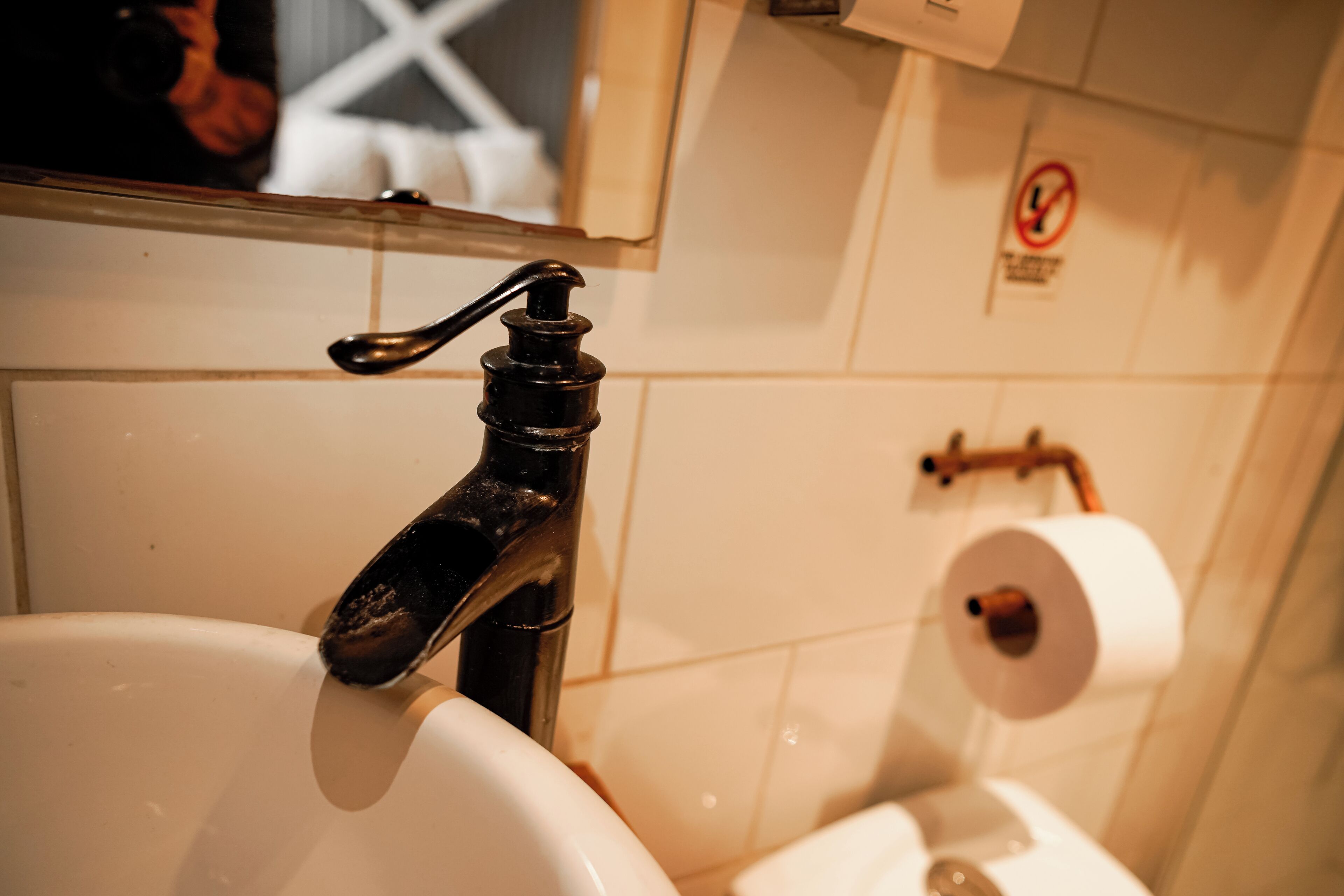 A bathroom sink with a faucet, a toilet paper holder, and a no-smoking sign on the wall.