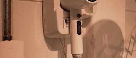 A hair dryer mounted on a wall with a coiled cord, a metal pipe, and a control panel.