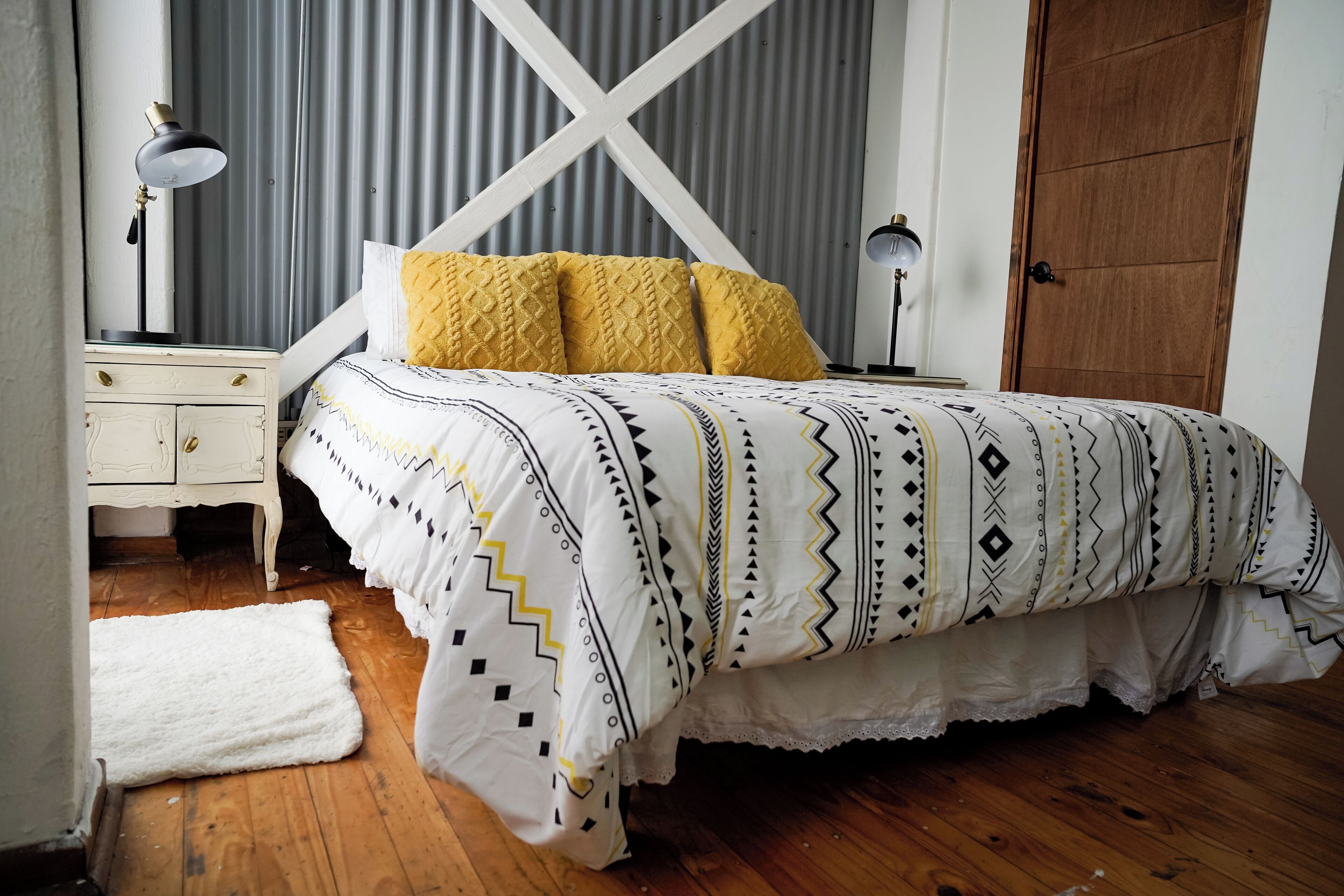 A bedroom with a bed, bedside tables, a lamp, a door, and a white rug.