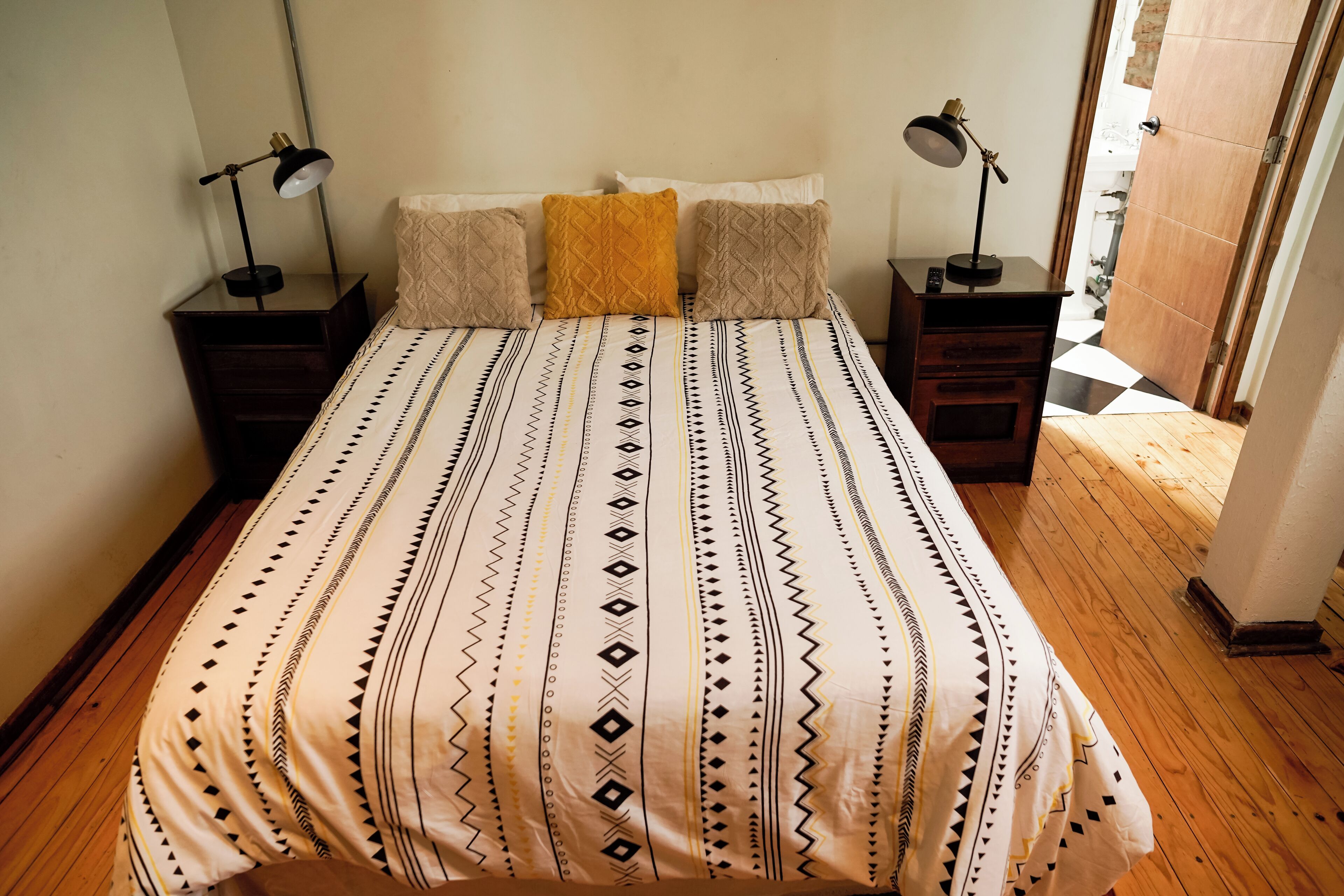 A bed with patterned bedding, two bedside tables with lamps, and a wooden floor.