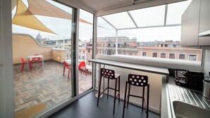 A modern kitchen with a large window, a dining area with red chairs, and a view of the cityscape. - Terrazza Giuliana (Rome)