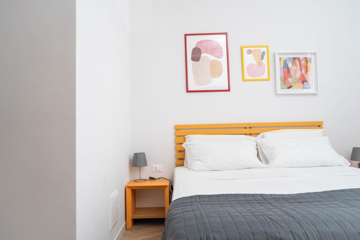 A neatly arranged bedroom with a bed, two bedside tables, and three framed artworks on the wall.