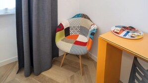 A corner room with a grey curtain, a colorful chair, a small table with a plate, and a mounted TV. - Terrazza Giuliana (Rome)
