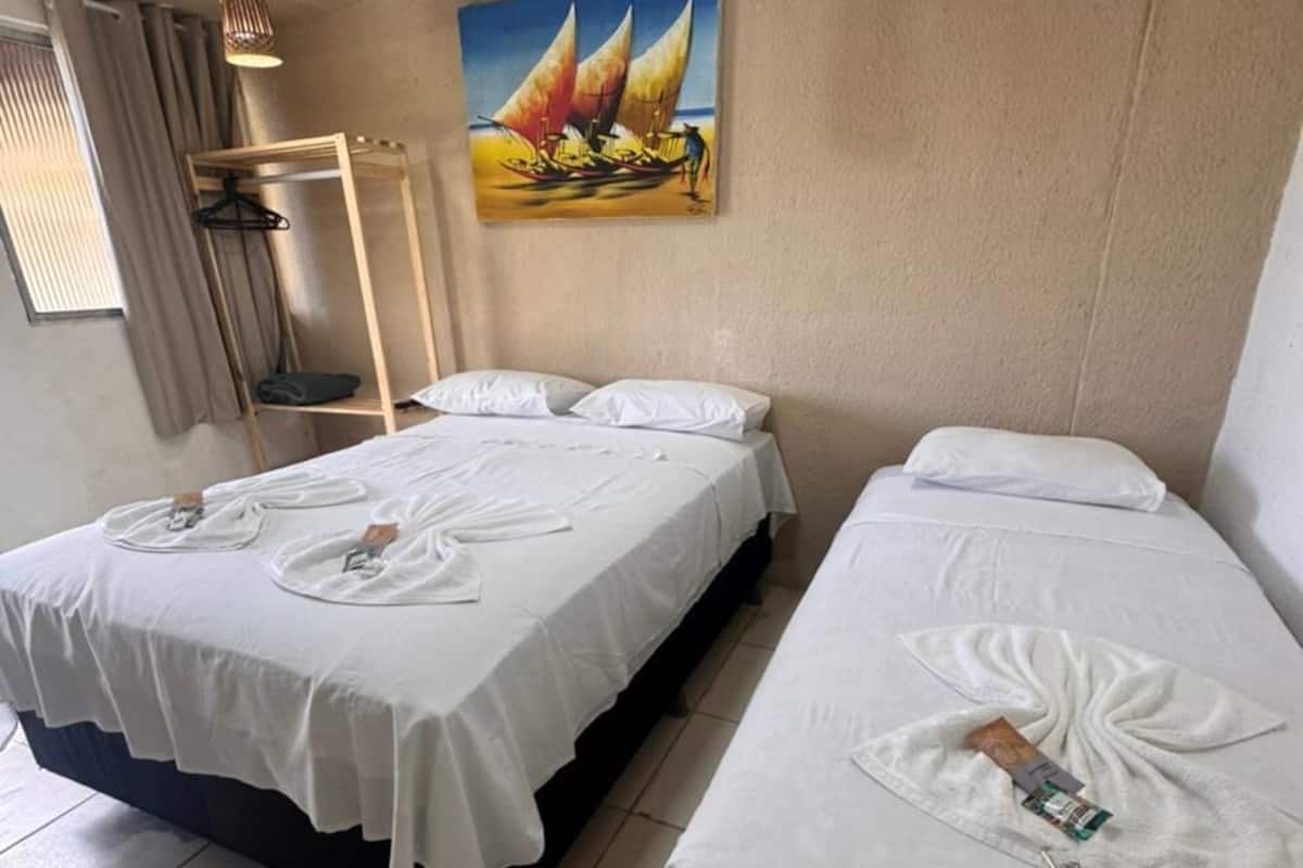 Ein Hotelzimmer mit zwei Betten, jedes mit einem Handtuch und einer Wasserflasche. An der Wand hängt ein Gemälde und es gibt ein Fenster mit Vorhängen.