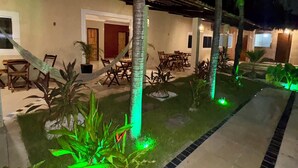 Un'area esterna ben illuminata con vialetto lastricato, palme e un edificio con tetto in tegole.