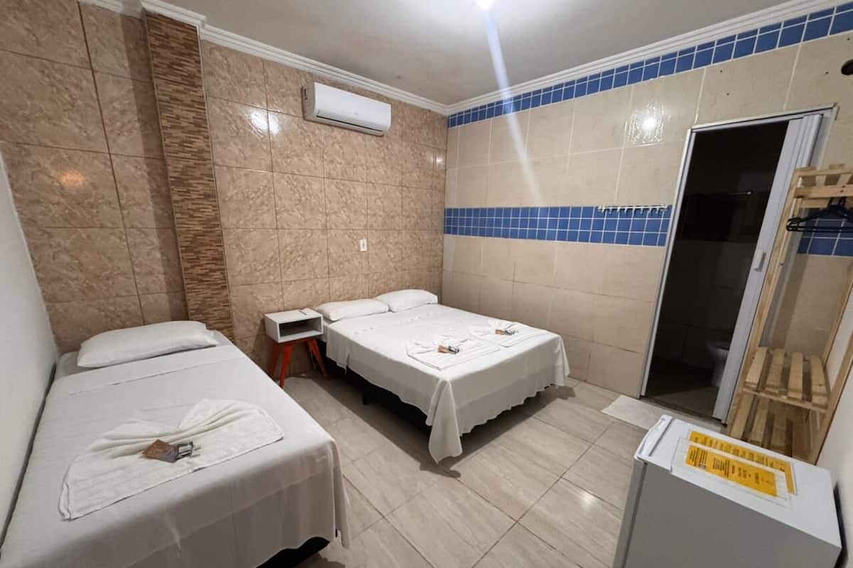 Ein Hotelzimmer mit zwei Betten, einem kleinen Tisch, einem Stuhl, einer Duschkabine und einem Kühlschrank.