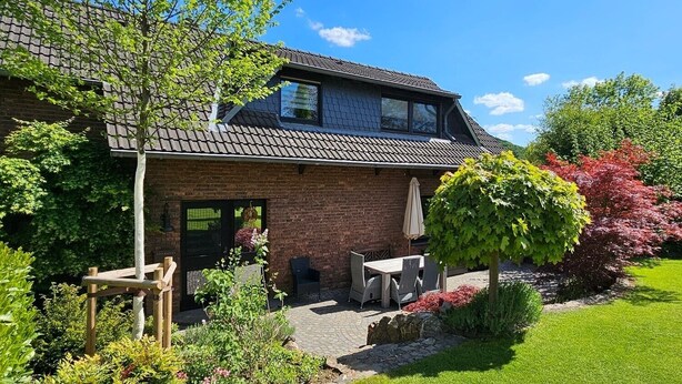 Een huis van baksteen met een pannendak, een voordeur en een klein terras met een tafel en stoelen.