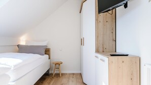 Een slaapkamer met een bed, een klein krukje, een houten kast en een televisie die aan de muur is bevestigd.