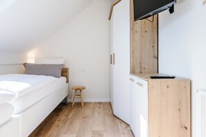 A bedroom with a bed, a small stool, a wooden cabinet, and a television mounted on the wall.