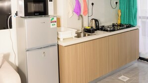 Cocina compacta equipada con microondas, refrigerador y estufa. Hay utensilios y una tetera en la encimera.