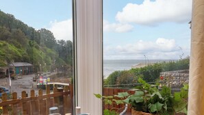 A view from a window overlooking a coastal area with a wooden fence, a bench, and a potted plant. - Zide the Zea (Ilfracombe)