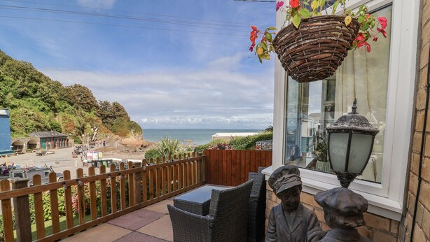 A balcony with wicker furniture, a hanging flower basket, and a statue. - Zide the Zea (Ilfracombe)
