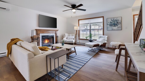 A modern living room with a fireplace, sofa, coffee table, and a dining area with chairs.