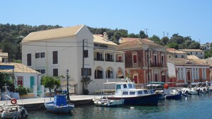 A coastal town with a marina, featuring a variety of buildings including a prominent white building with a balcony and a red building with a classical facade.