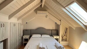 A bedroom with a sloped ceiling, a skylight, a bed with neatly folded towels, a bedside table, and a wardrobe.
