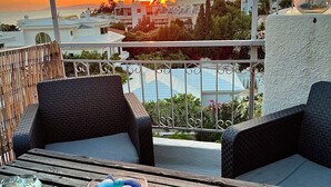 A balcony with wicker furniture, a table with a bowl of eggs, and a view of the sunset over a cityscape. - Exclusive Penthouse Apt at Glyfada Marina &Beach, 2 min walk to shopping, dining (Glifada)