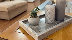 A modern living room with a beige sofa, a small potted plant, and three candles on a glass tray. - Exclusive Penthouse Apt at Glyfada Marina &Beach, 2 min walk to shopping, dining (Glifada)