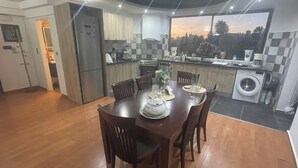 A modern kitchen with a dining area, featuring a large window, wooden cabinets, and a built-in washing machine. - Exclusive Penthouse Apt at Glyfada Marina &Beach, 2 min walk to shopping, dining (Glifada)
