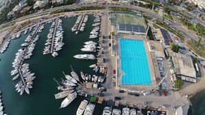 An aerial view of a marina with numerous boats docked, a large swimming pool, and adjacent buildings. - Exclusive Penthouse Apt at Glyfada Marina &Beach, 2 min walk to shopping, dining (Glifada)