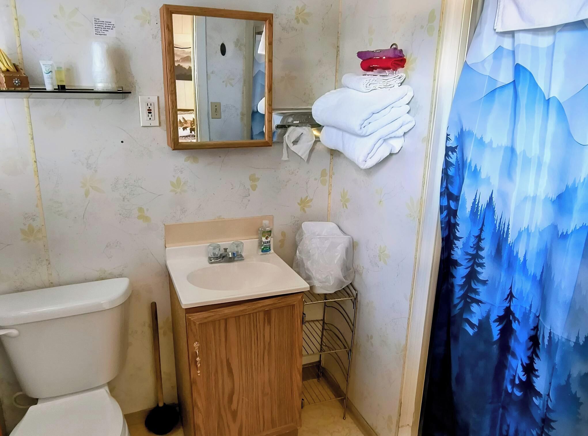 Un baño con inodoro, lavabo, espejo y cortina de ducha con diseño de bosque.